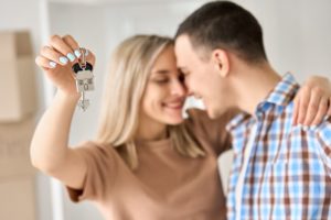 Młodzi kobieta i mężczyzna w nowym mieszkaniu, ona trzyma kluczyki z brelokiem w kształcie domu