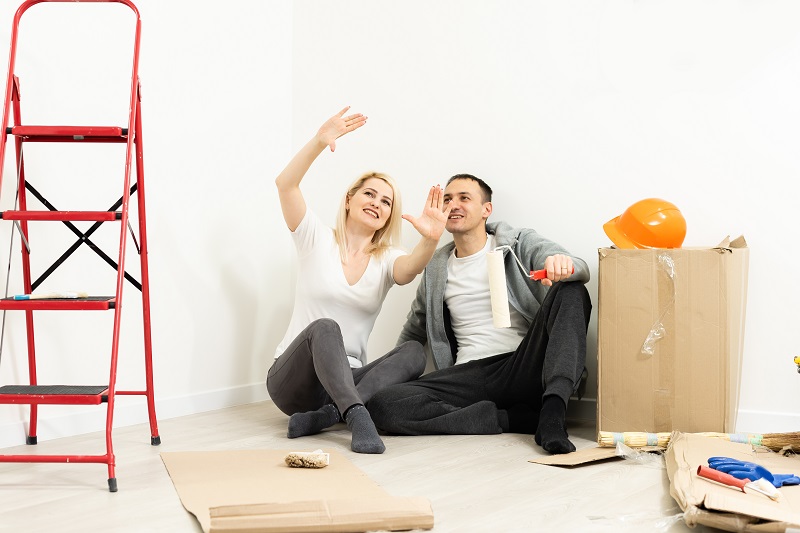 Kobieta i mężczyzna siedzą na podłodze w remontowanym mieszkaniu, kobieta gestykulując, pokazuje coś mężczyźnie