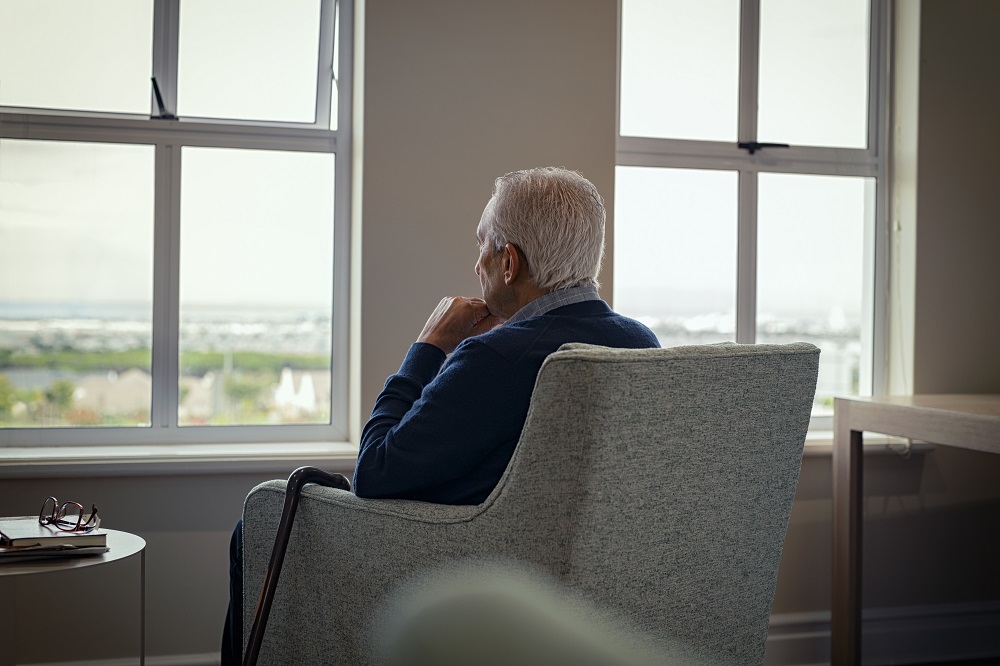 Stary mężczyzna siedzi w fotelu, patrząc w stronę okien