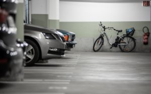 Podziemny parking, dwa zaparkowane samochody, rower oparty o ścianę, gaśnica