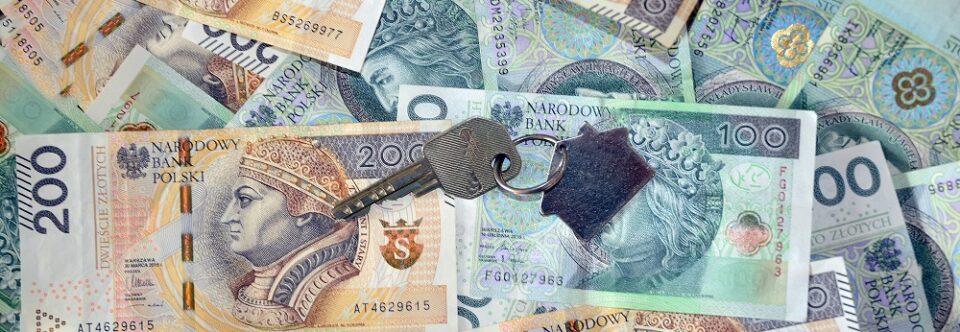 Powierzchnia utworzona z polskich banknotów, na której leży klucz z brlokiem w kształcie domu