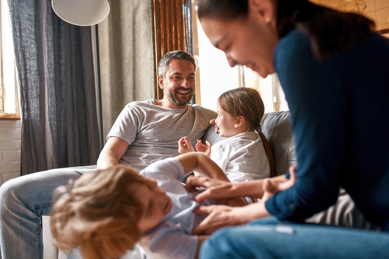 Kobieta, mężczyzna i dwoje małych dzieci siedzą na sofie, śmieją się